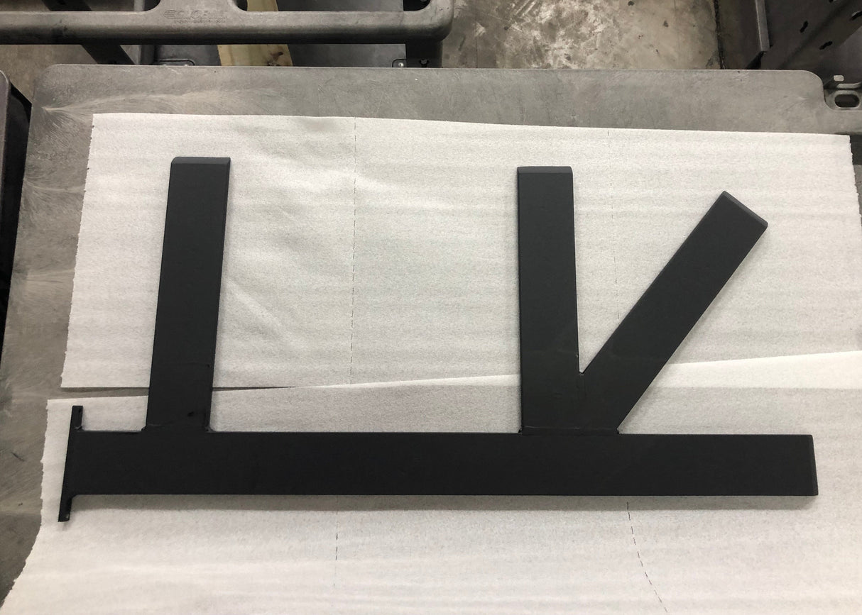 A Black Custom Support Bracket with two arms coming out horizontally at a 90-degree angle and one arm at a 45-degree angle, laying on packing paper on a concrete floor.