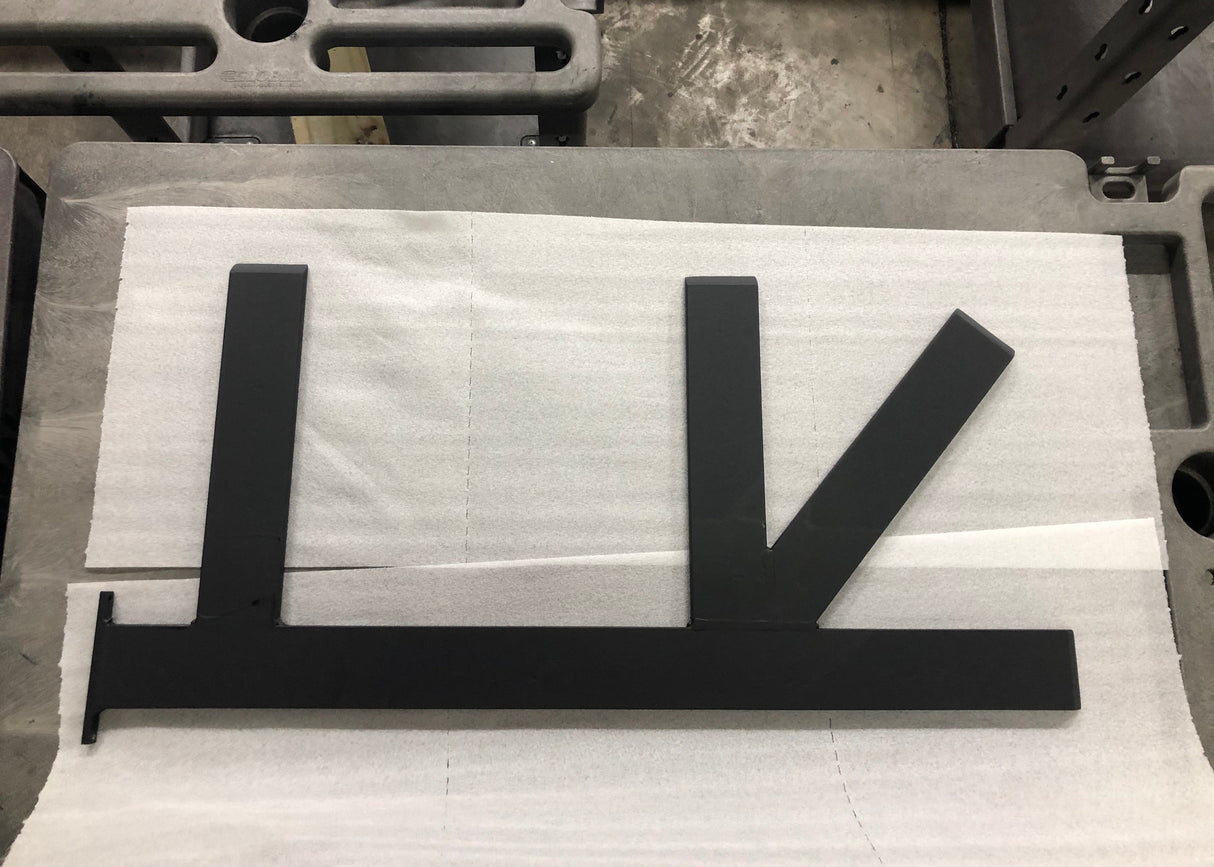 A Black Custom Support Bracket with two arms coming out horizontally at a 90-degree angle and one arm at a 45-degree angle, laying on packing paper on a concrete floor.