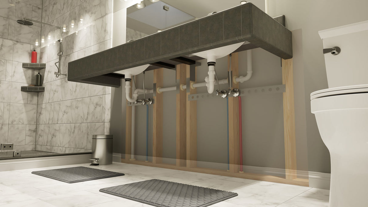 A right-angle view of a floating dark gray vanity with two sinks with two gray bathmats on the floor beneath it, a white toilet in the foreground and a standing shower in the background.