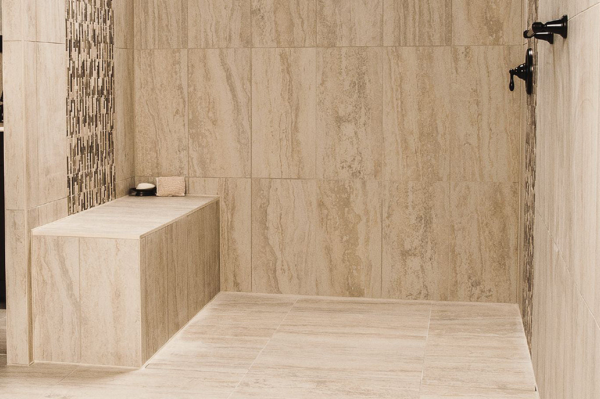 A sand-colored tiled standing shower with a full-sized Schluter waterproof shower bench holding a bar of soap and loofah.