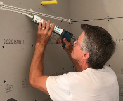 A man in a white shirt using a GoBoard Sealant tube to distribute adhesive on a GoBoard Building Panel.