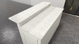 A top-down view of a white marble kitchen island with a countertop overhang on a gray tile floor.